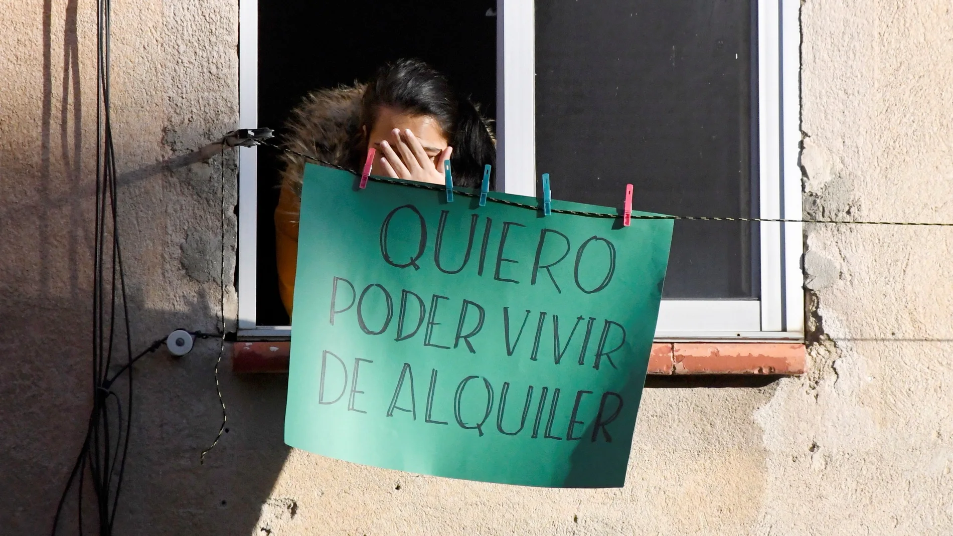 Una vecina del edificio donde se ha impedido un desahucio en Segovia este miércoles cuelga un cartel en su ventana en el que se lee "quiero poder vivir de alquiler".