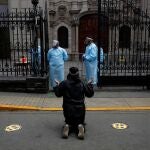 A woman kneels on the street while praying near security personnel of the Monastery of the Nazarenes, dressed in personel protective equipment (PPE), as churches continue to be closed due to the coronavirus disease (COVID-19) outbreak, in Lima, Peru October 7, 2020. REUTERS/Sebastian Castaneda NO RESALES. NO ARCHIVES