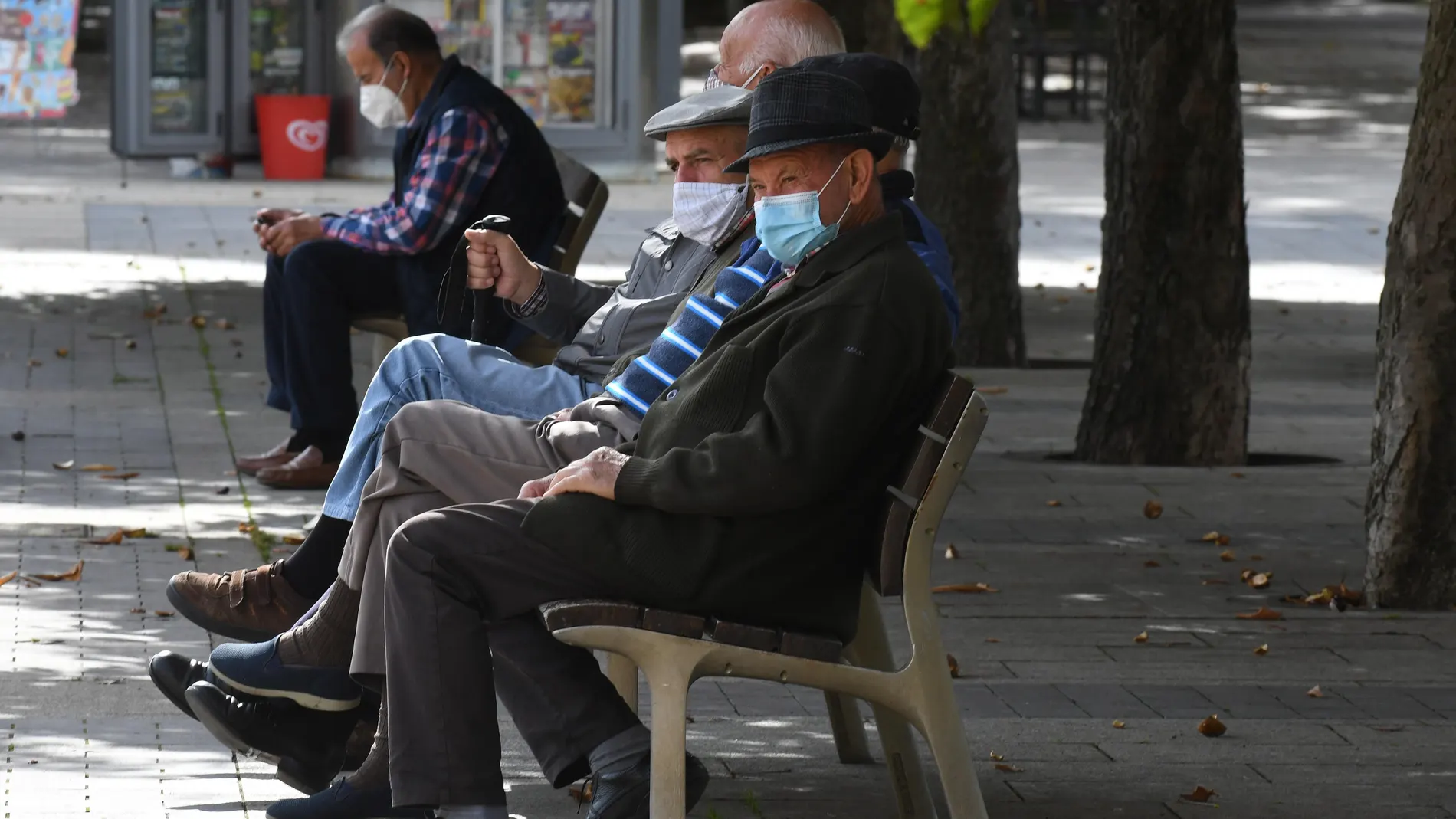 Varias personas descansan en un banco protegidos con mascarilla en León