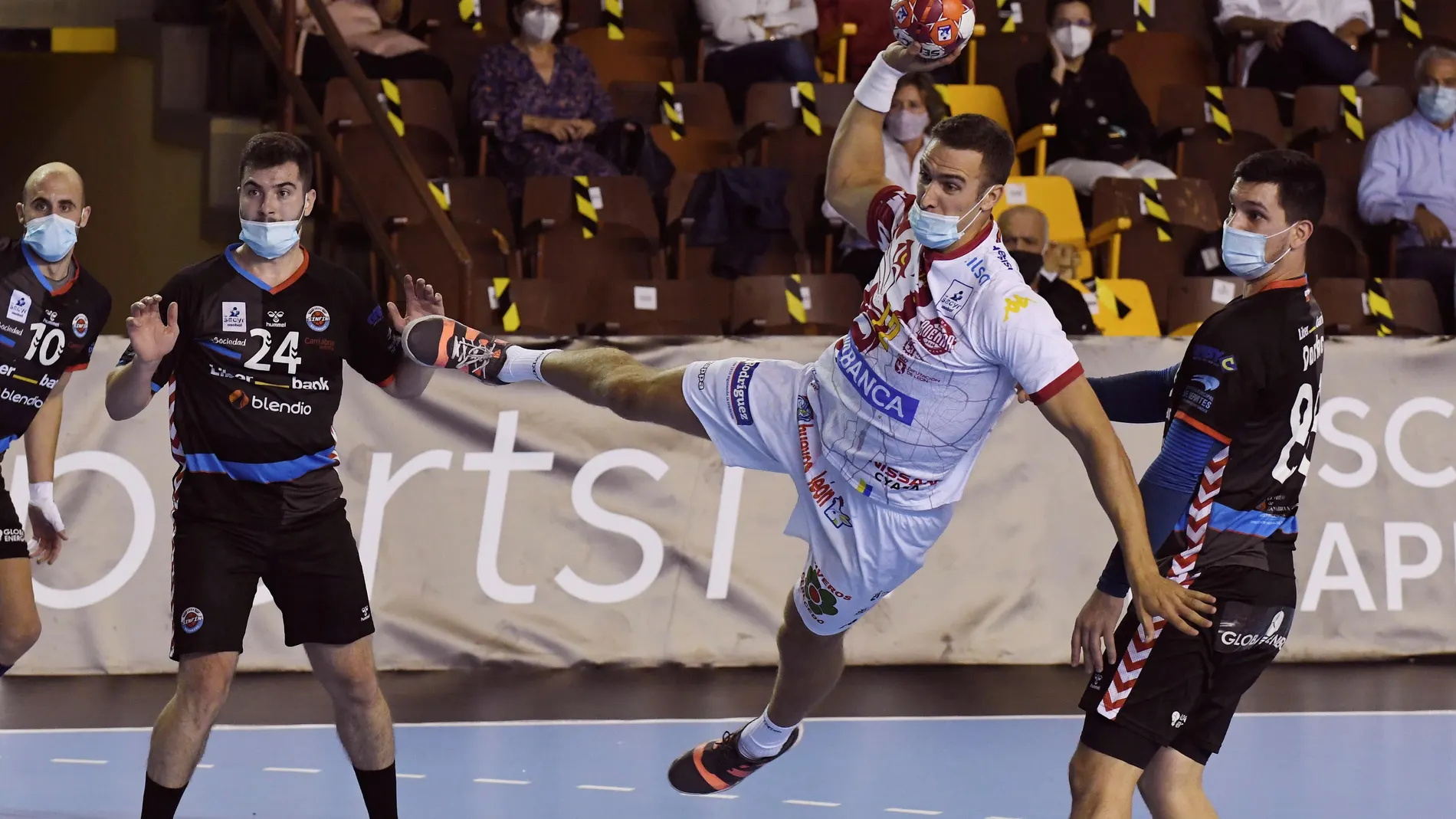 El jugador del Abanca Ademar Drew Donlin (c) lanza ante los jugadore del Sinfín Liberbank durante el partido de la octava jornada de la Liga Sacyr ASOBAL disputado hoy en el palacio municipal de deportes de León. Los jugadores de ambos equipos tuvieron que disputar el encuentro provistos de mascarilla debido a las medidas sanitarias impuestas por la Junta de Castilla y León para frena la expansión de la pandemia de la cpvid-19. EFE/ J.casares