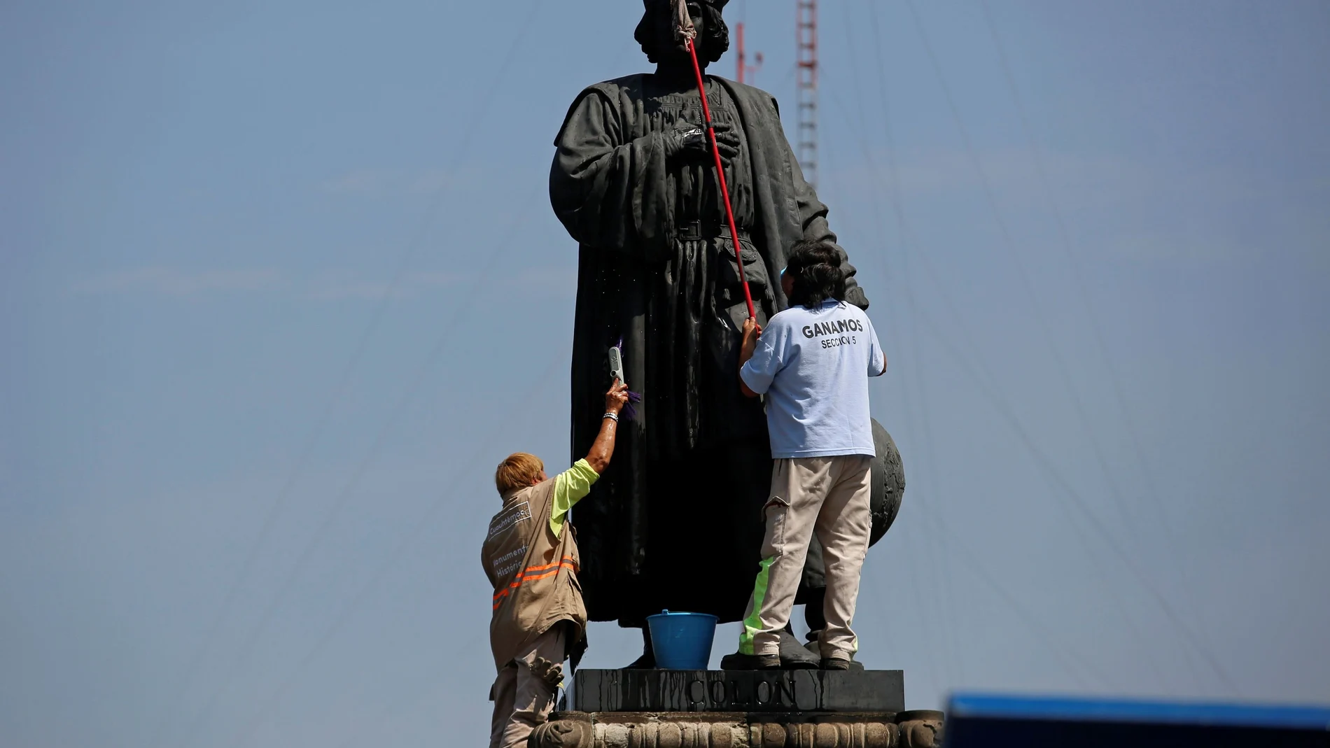 Trabajadores limpian una pintada en la escultura de Colón en México antes de que fuera retirada en octubre de 2020
