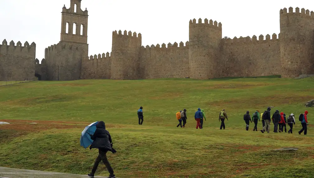 Una persona se protege de la lluvia junto a la muralla de Ávila