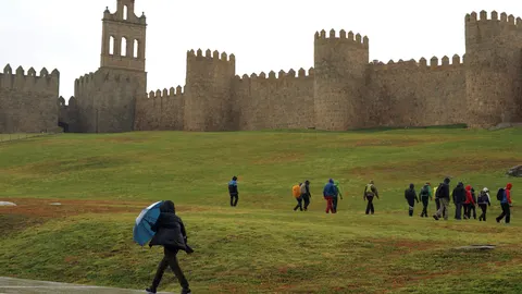 Una persona se protege de la lluvia junto a la muralla de Ávila