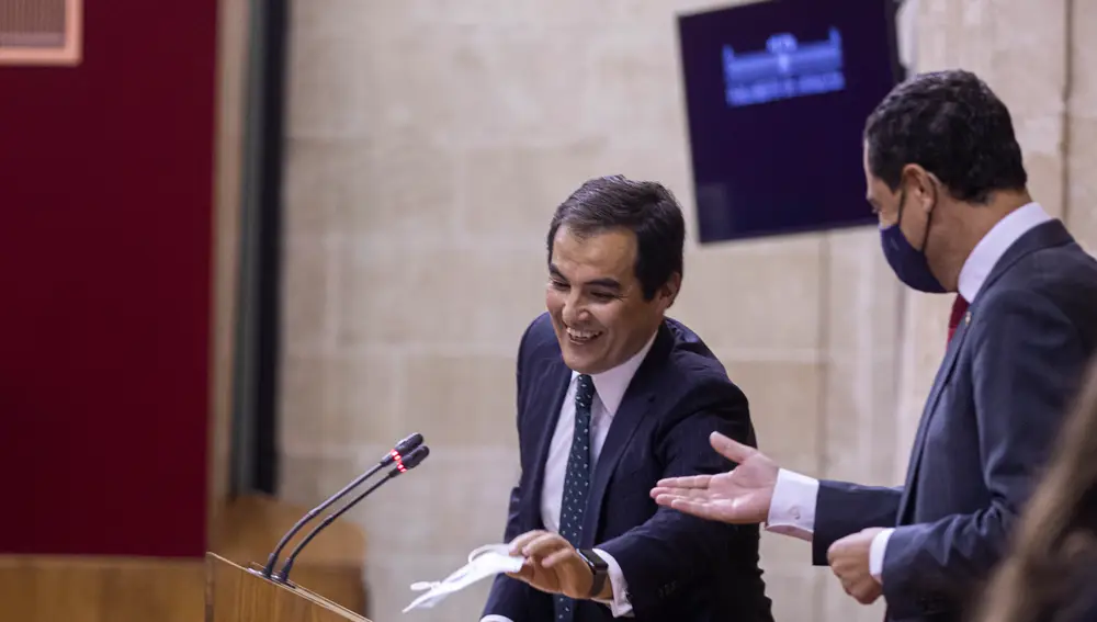 El portavoz del grupo parlamentario popular, José Antonio Nieto (i), junto al presidente de la Junta de Andalucía, recoge su mascarilla tras olvidarla en el estrado durante su intervención en la segunda jornada del Debate sobre el Estado de la Comunidad