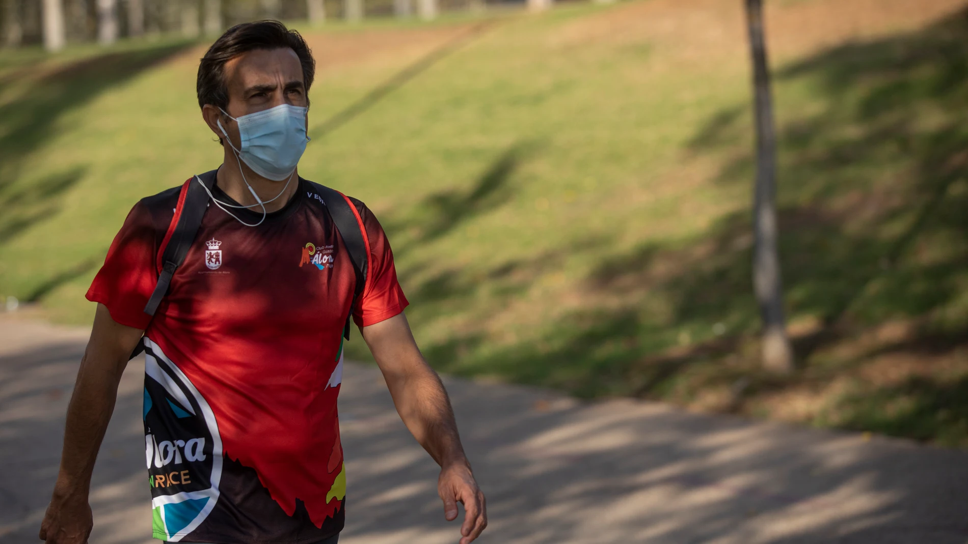Un hombre con mascarilla y ropa deportiva camina por un parque sevillano