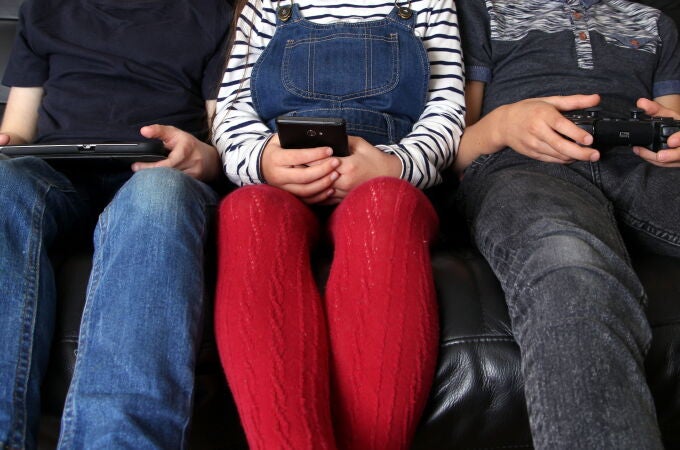 Tres niños con diferentes pantallas: tableta, móvil y un mando de videojuegos