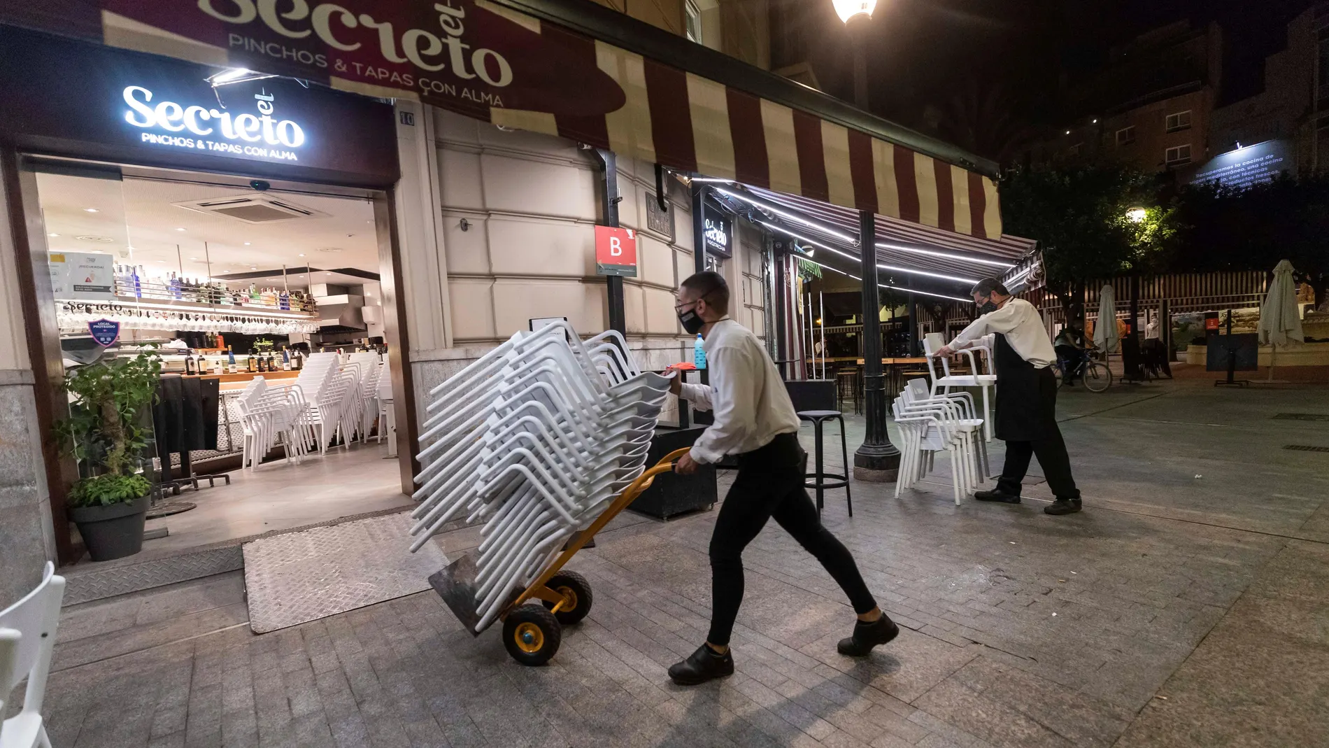 Dos camareros recogen las sillas de la terraza de un bar de la Plaza de Las Flores de Murcia. EFE/Marcial Guillén
