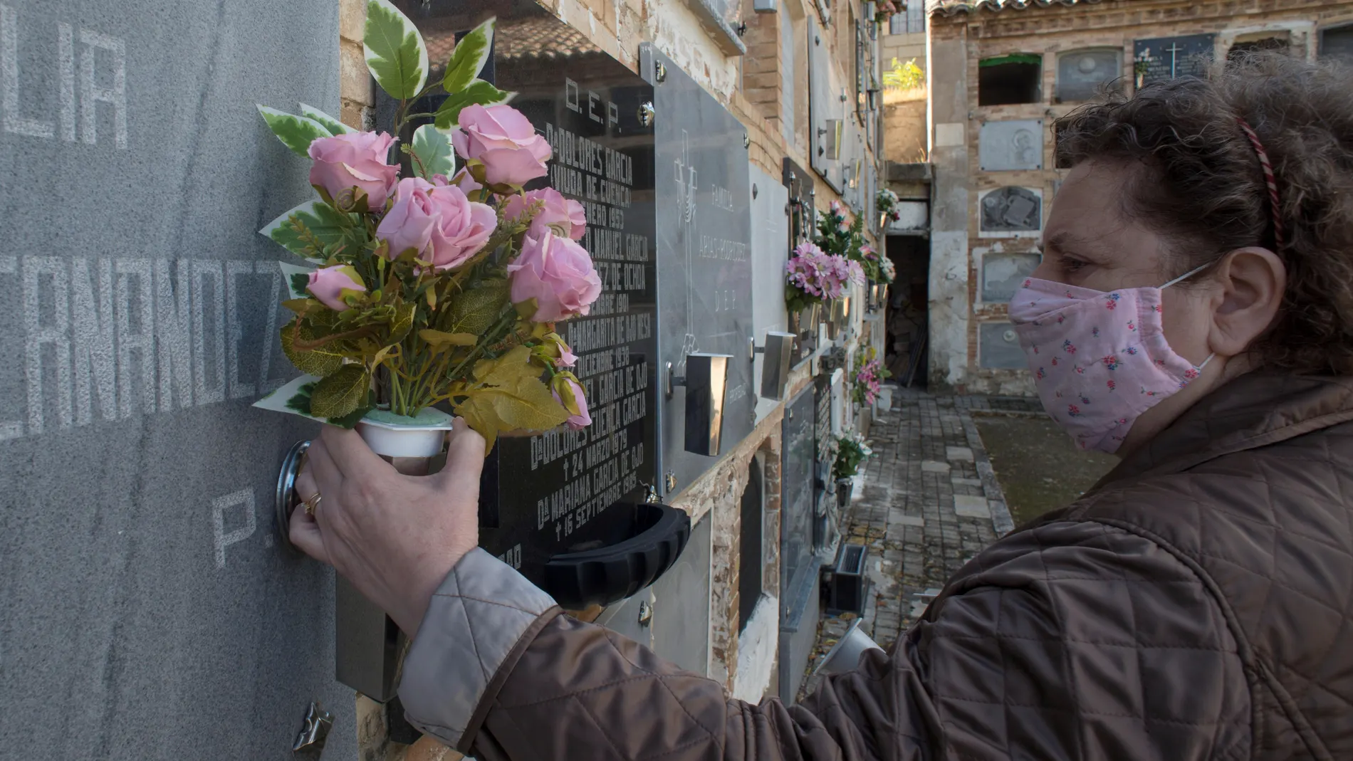 Una mujer coloca flores de plástico en la lápida de un familiar en el cementerio de San Eufrasio de Jaén. EFE/José Manuel Pedrosa.