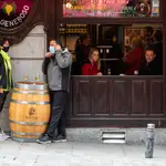 Imagen de un bar en el que dos personas con mascarillas toman una cerveza en el exterior, y a su lado dos sin mascarillas en el interior a través de una ventana abierta hacen los mismo.