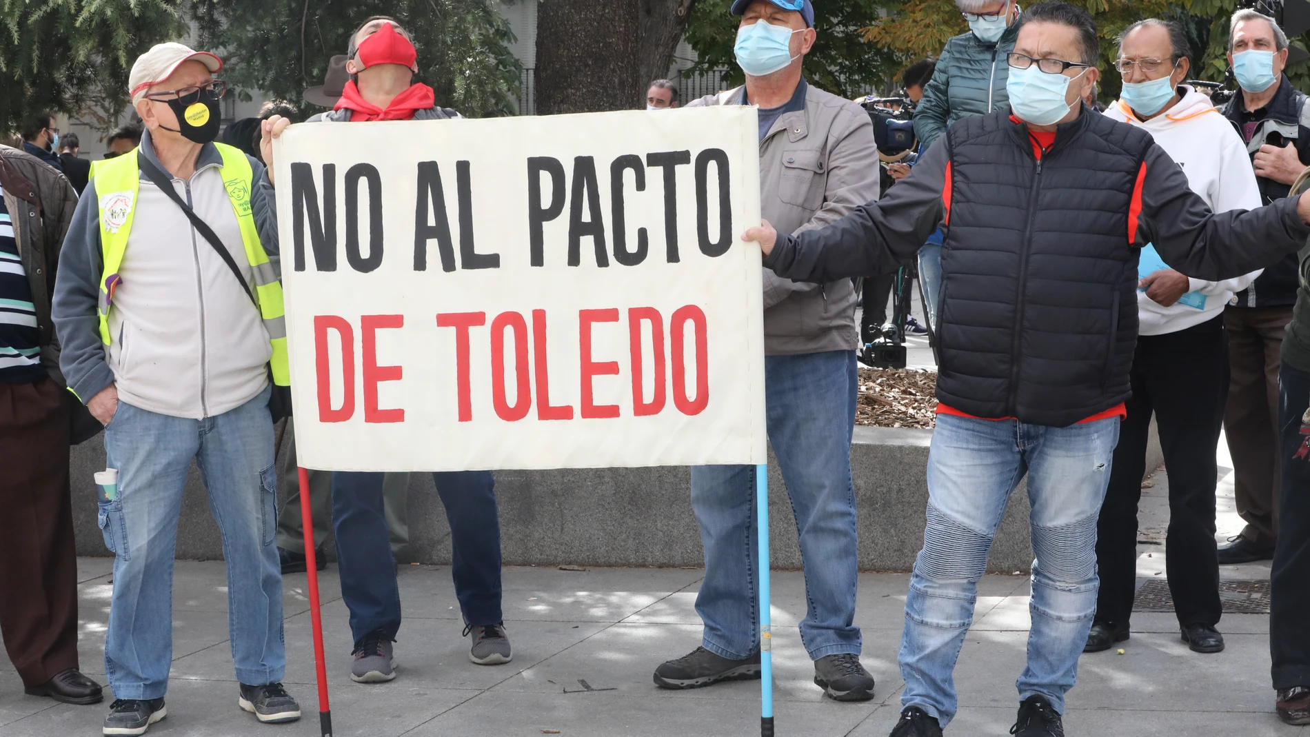 Un grupo de personas sostiene una pancarta donde se puede leer "No al pacto de Toledo" en las inmediaciones del Congreso de los Diputado