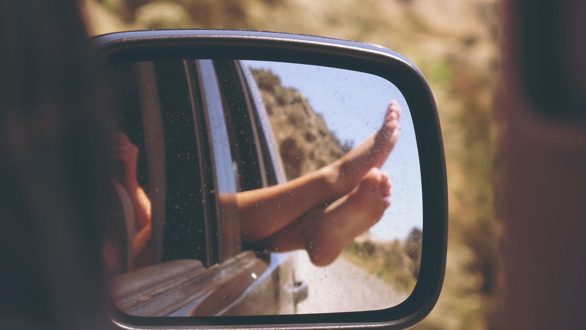 En la imagen, una mujer saca los pies por la ventanilla del coche.