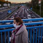 Una mujer camina con mascarilla sobre la carretera de circunvalación M30 atascada a primera hora de la mañana.