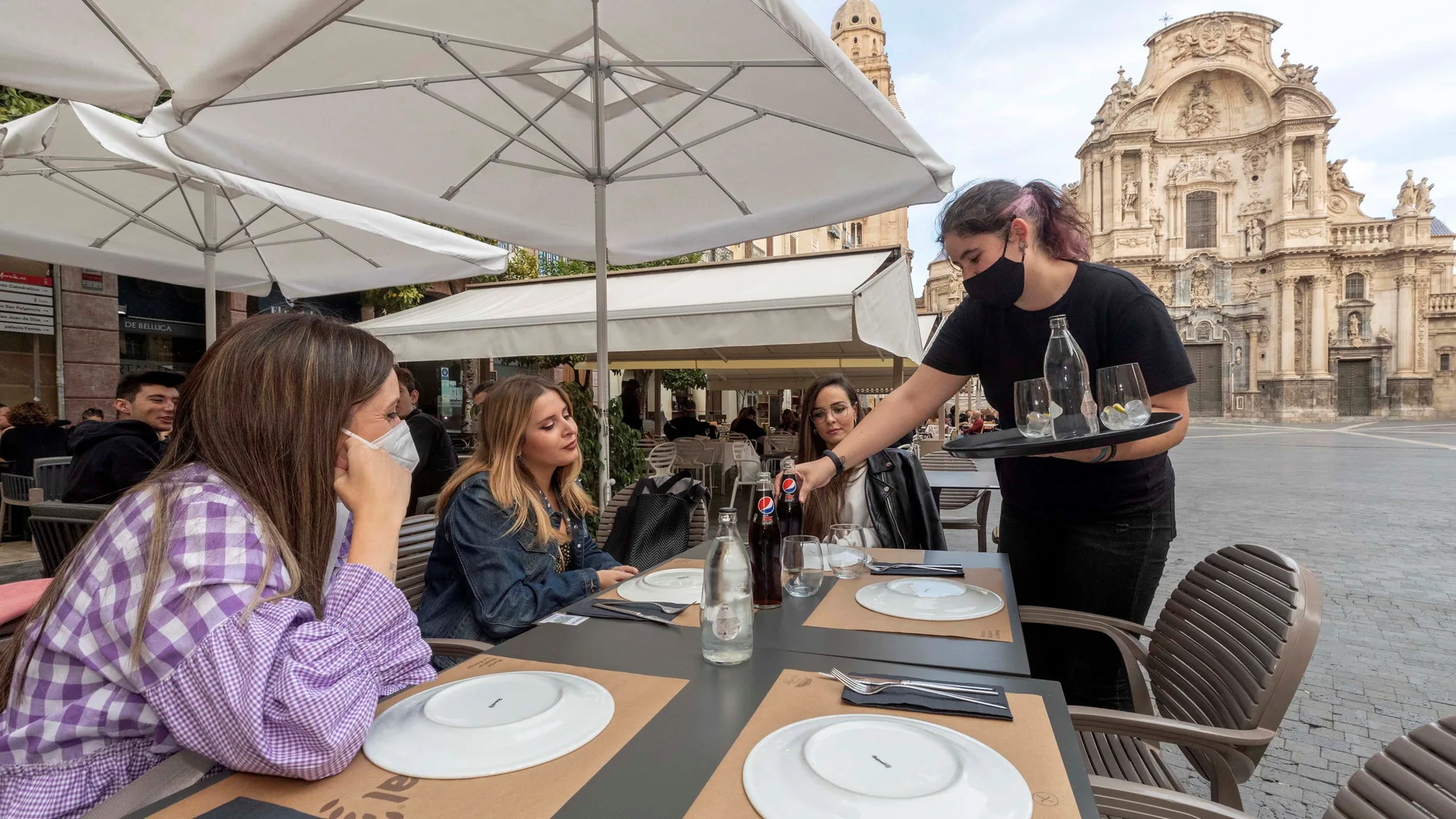 Una camarera sirve la bebida en la mesa de la terraza de un restaurante en la Plaza Cardenal Belluga de Murcia