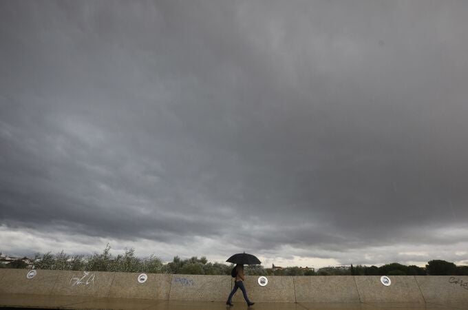 Una persona se resguarda de la lluvia con un paraguas bajo un cielo negro en Córdoba