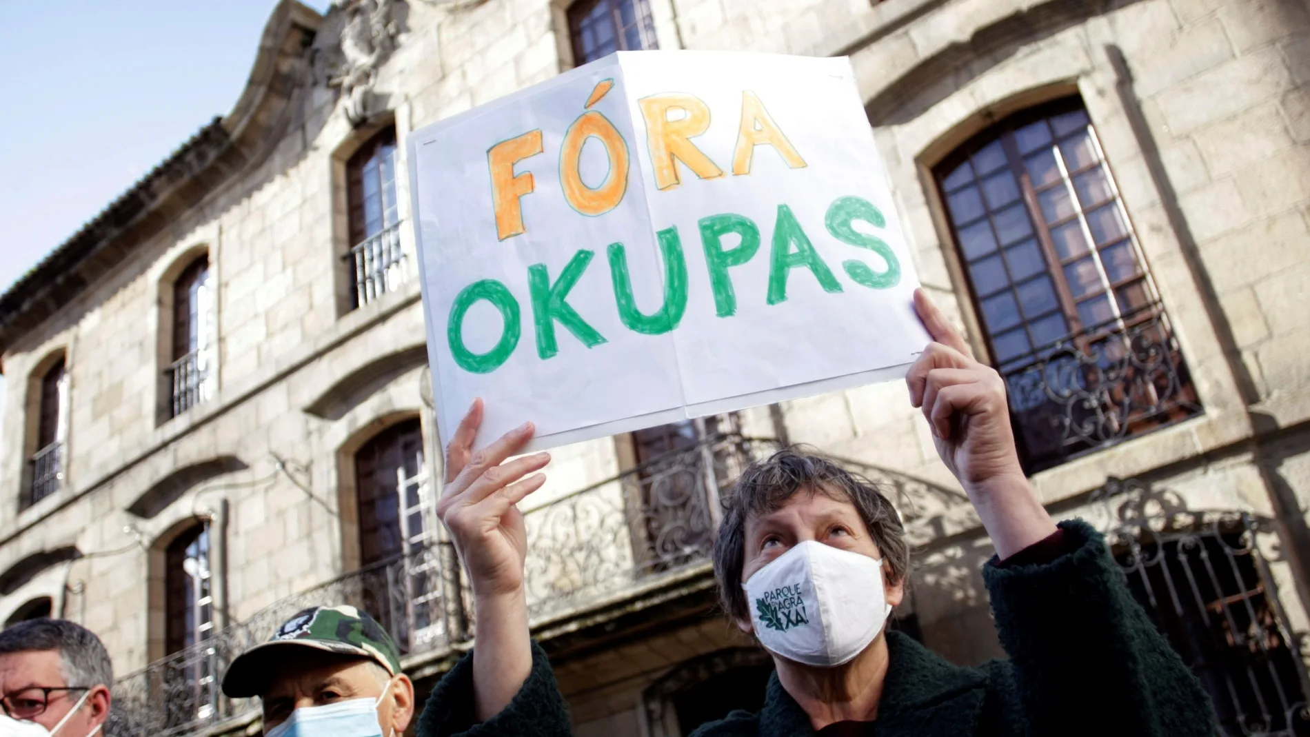 Una mujer sostiene una cartel con la frase "fuera okupas"