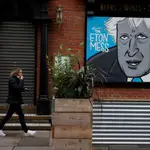 A woman walks past a caricature of Britain&#39;s Prime Minister Boris Johnson in the boarded up window of a closed pub in Manchester, Britain, November 10, 2020. REUTERS/Phil Noble NO RESALES. NO ARCHIVES.