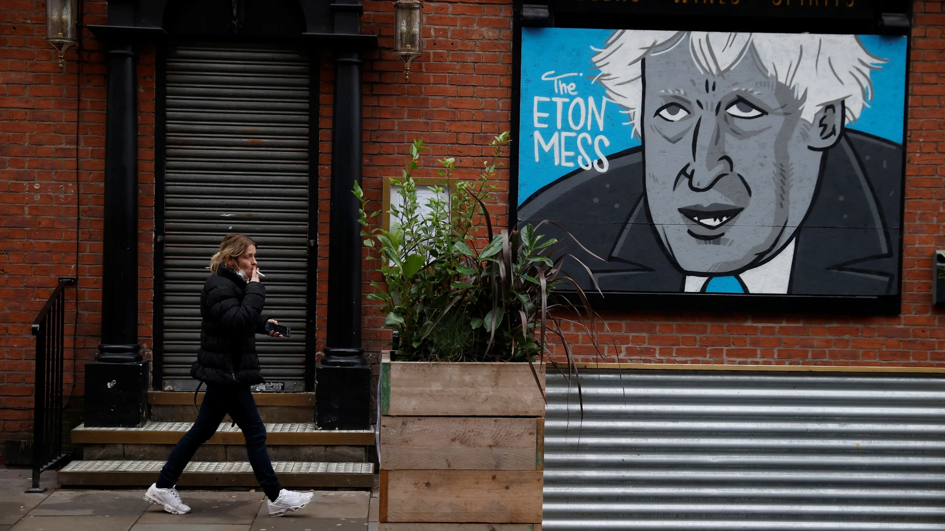 A woman walks past a caricature of Britain's Prime Minister Boris Johnson in the boarded up window of a closed pub in Manchester, Britain, November 10, 2020. REUTERS/Phil Noble NO RESALES. NO ARCHIVES.
