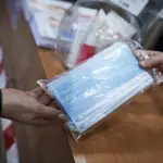 Una farmacéutica enseña a un cliente un paquete de mascarillas en la farmacia