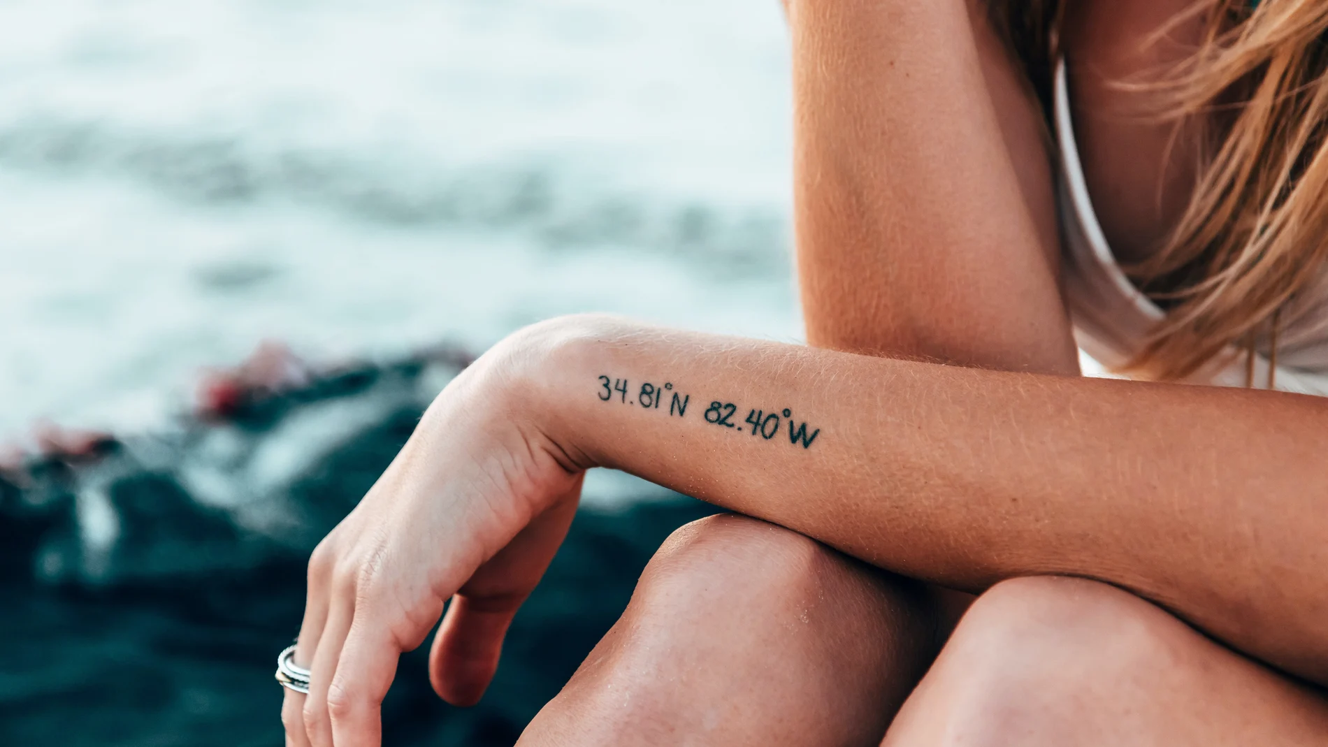 En la imagen, una chica presume de sus tatuajes frente al mar.