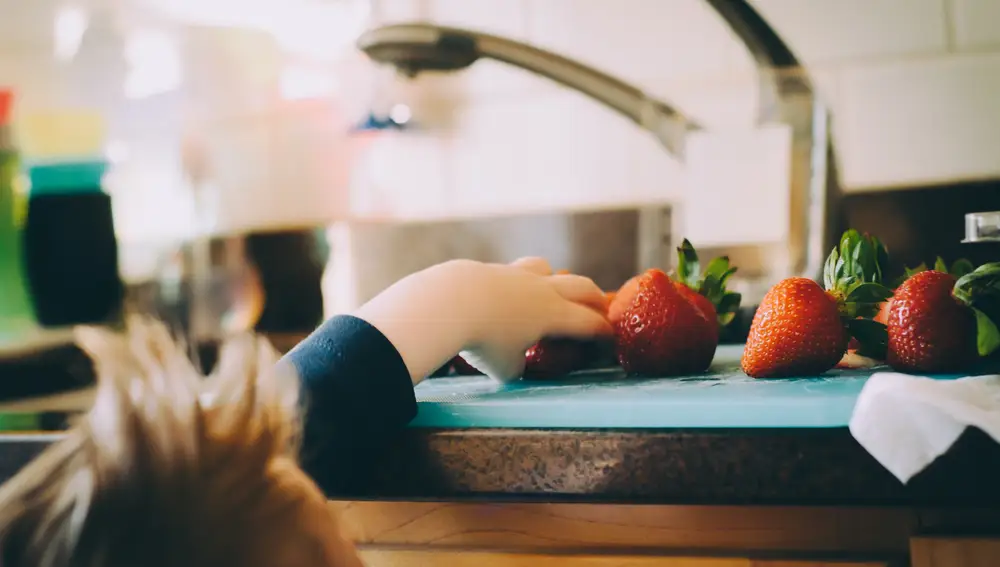 En la imagen, un niño intenta alcanzar unas fresas en la cocina.
