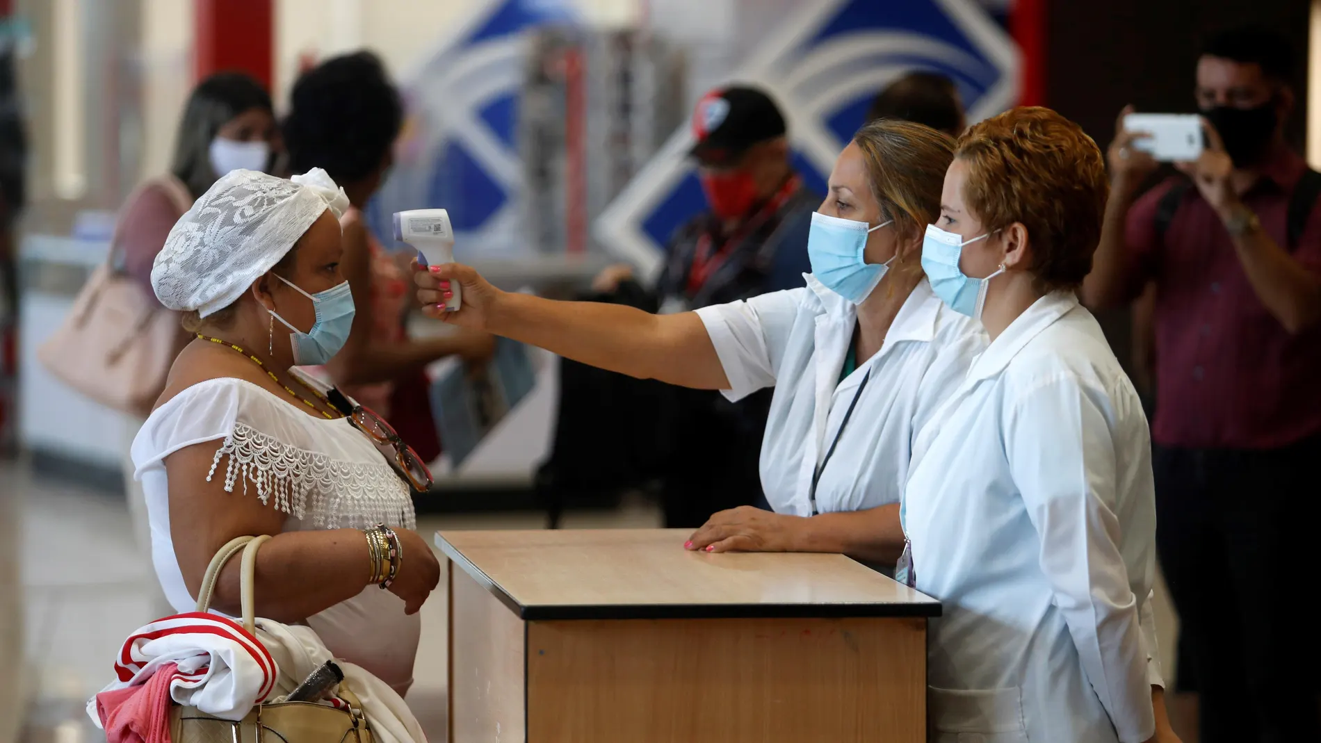 AME8519. LA HABANA (CUBA), 15/11/2020.- Trabajadoras del aeropuerto de La Habana toman la temperatura a una mujer en el primer día que reinicia las operaciones, suspendidas desde hace meses a causa de la pandemia, hoy en La Habana (CUBA). EFE/ Yander Zamora