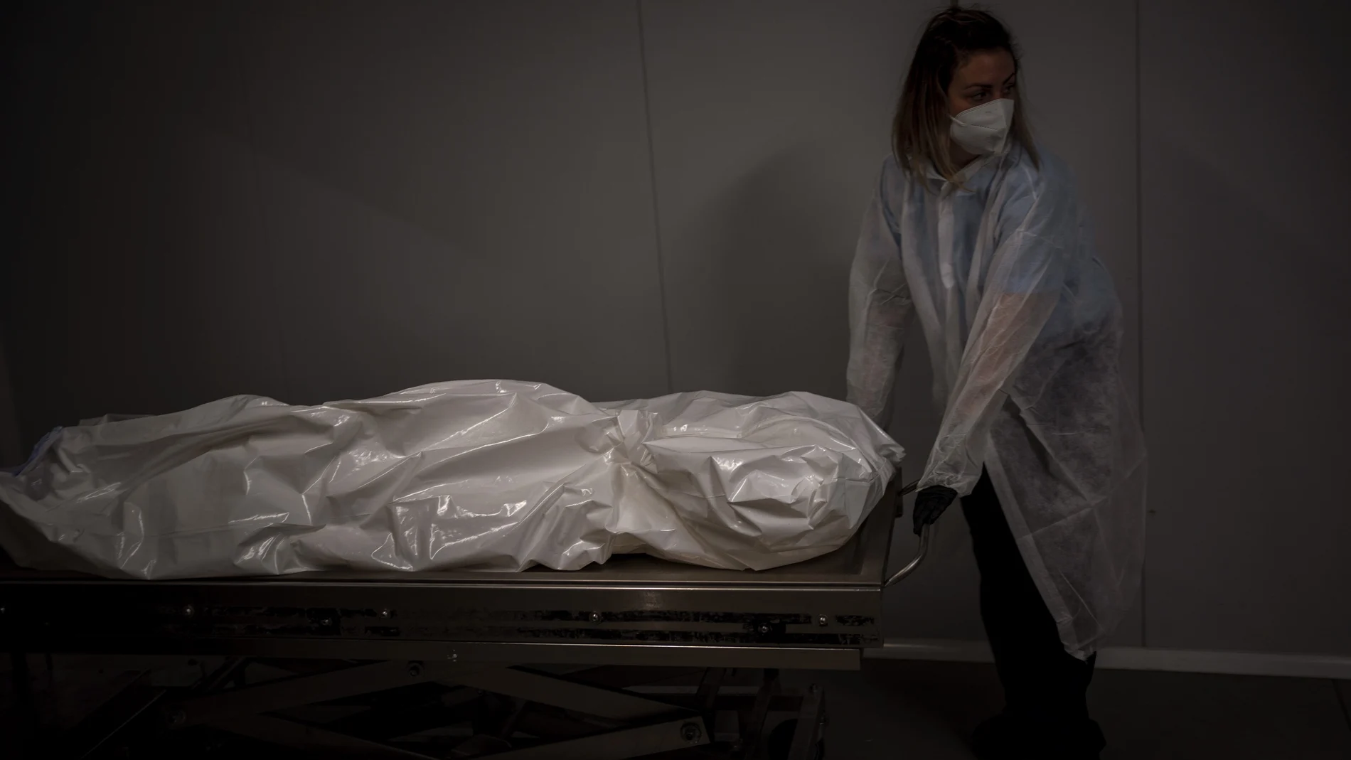Un trabajador funerario transporta el cuerpo de una persona fallecida por COVID - 19 en una morgue de Barcelona hoy.
