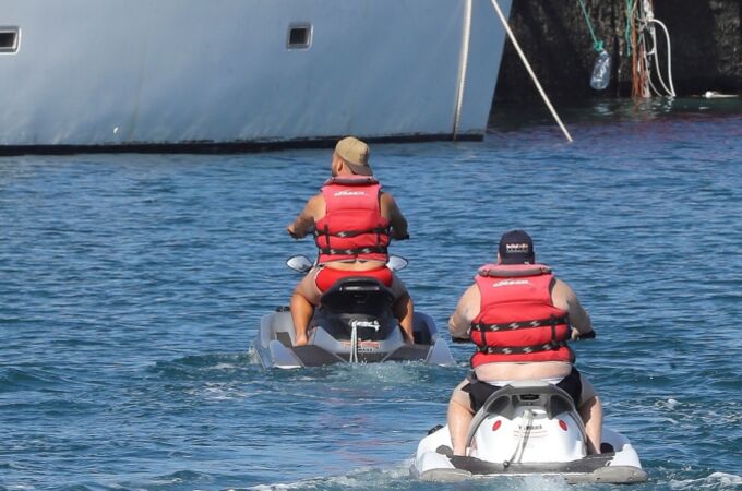 Dos turistas en motos de agua pasan junto al muelle de Arguineguín, donde se hacinan más de 1.700 inmigrantes