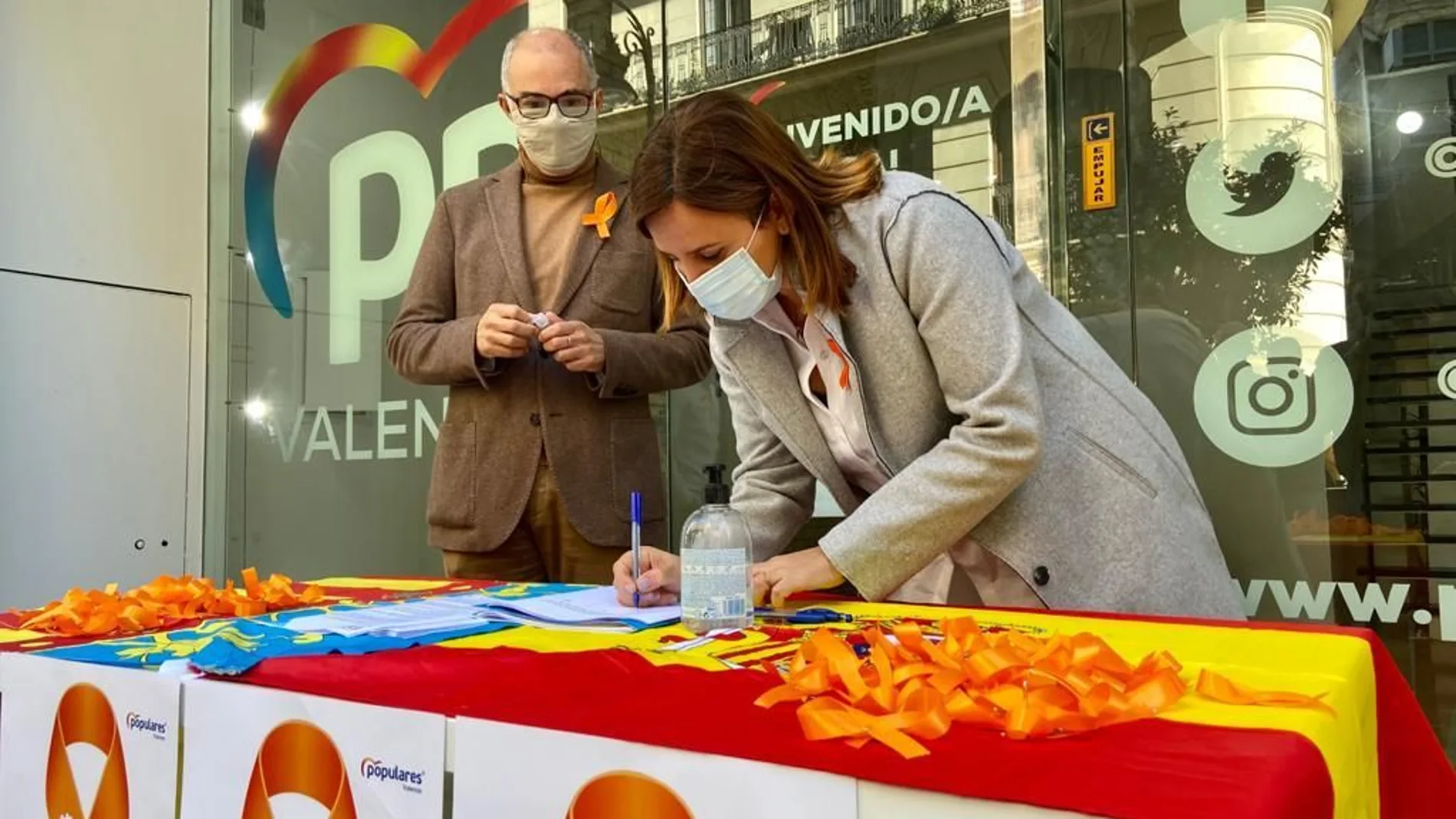 María José Catalá firma ante la atenta mirada del senador Fernando de Rosa