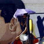 Una mujer camina bajo su paraguas frente a un mural con la imagen del presidente de Venezuela, Nicolás Maduro, en la ciudad de Guacara, en el norte del país.23/11/2020