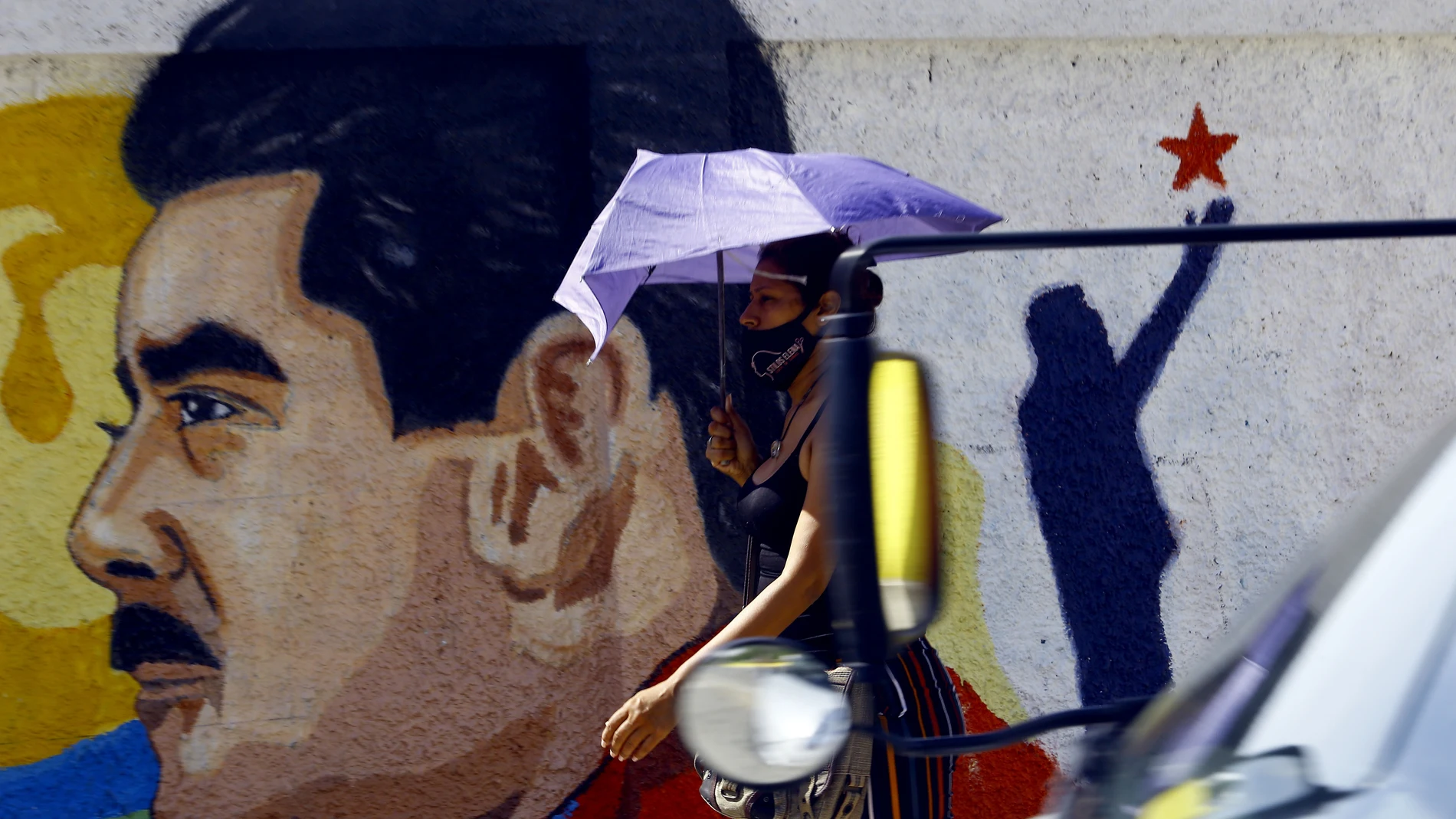 Una mujer camina bajo su paraguas frente a un mural con la imagen del presidente de Venezuela, Nicolás Maduro, en la ciudad de Guacara, en el norte del país.23/11/2020