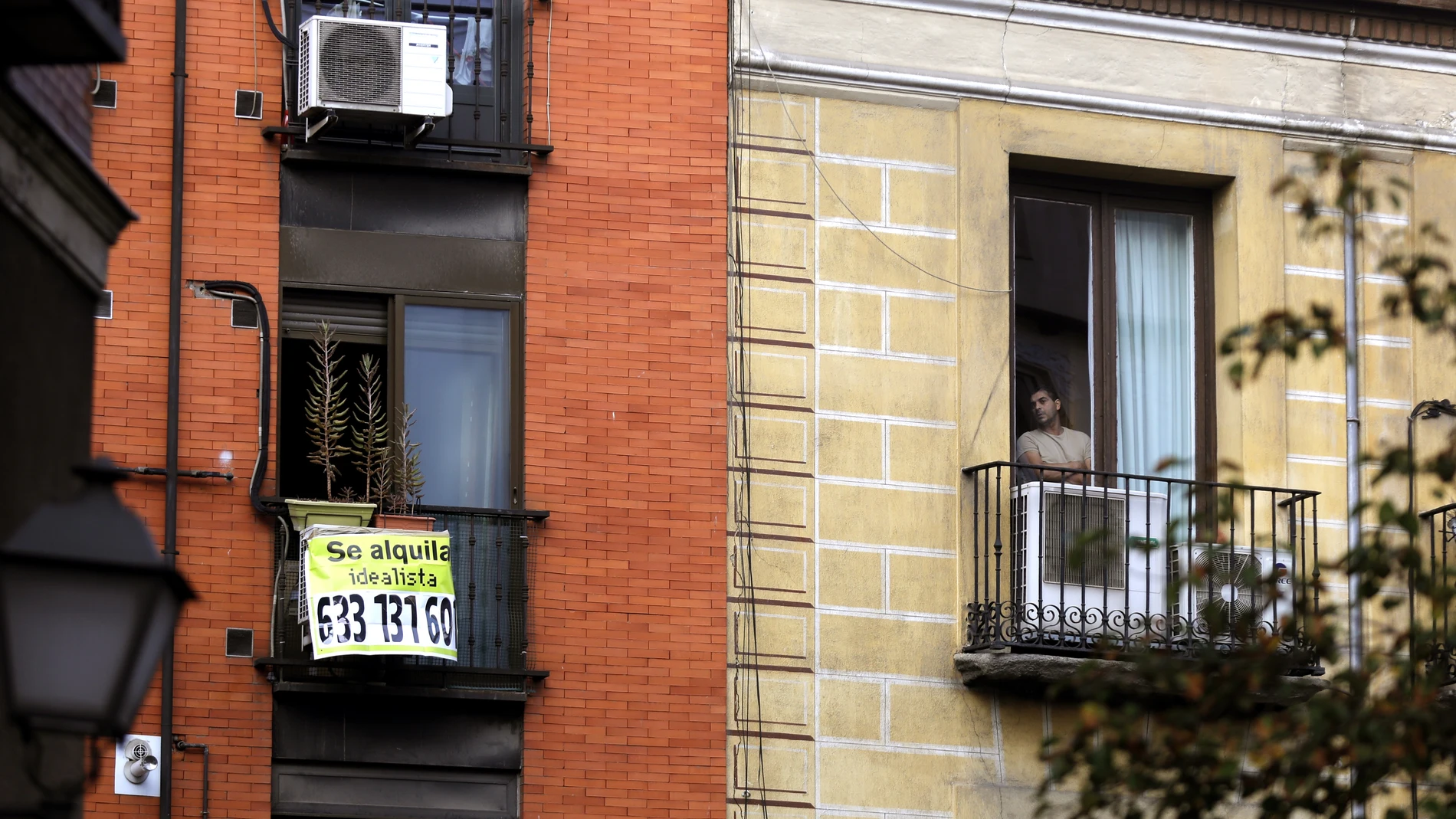 Dos balcones en el que en uno de ellos se ve un cartel de "se alquila" y en el otro una persona