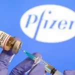 FILE PHOTO: A woman holds a small bottle labeled with a &quot;Coronavirus COVID-19 Vaccine&quot; sticker and a medical syringe in front of displayed Pfizer logo in this illustration taken, October 30, 2020. REUTERS/Dado Ruvic/File Photo