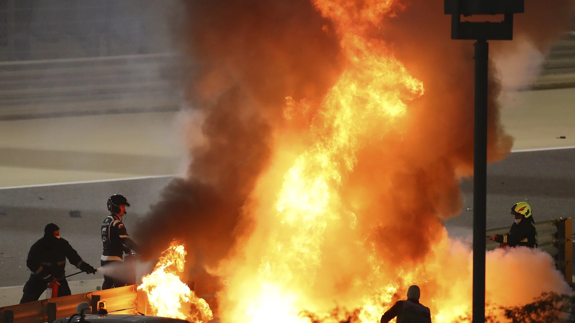 Staff extinguish flames from Haas driver Romain Grosjean of France's car after a crash during the Formula One race in Bahrain International Circuit in Sakhir, Bahrain, Sunday, Nov. 29, 2020. (Brynn Lennon, Pool via AP)