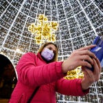 Una mujer se fotografía con mascarilla bajo la iluminación navideña