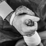 Un médico sostiene la mano de un paciente ingresado en la UCI