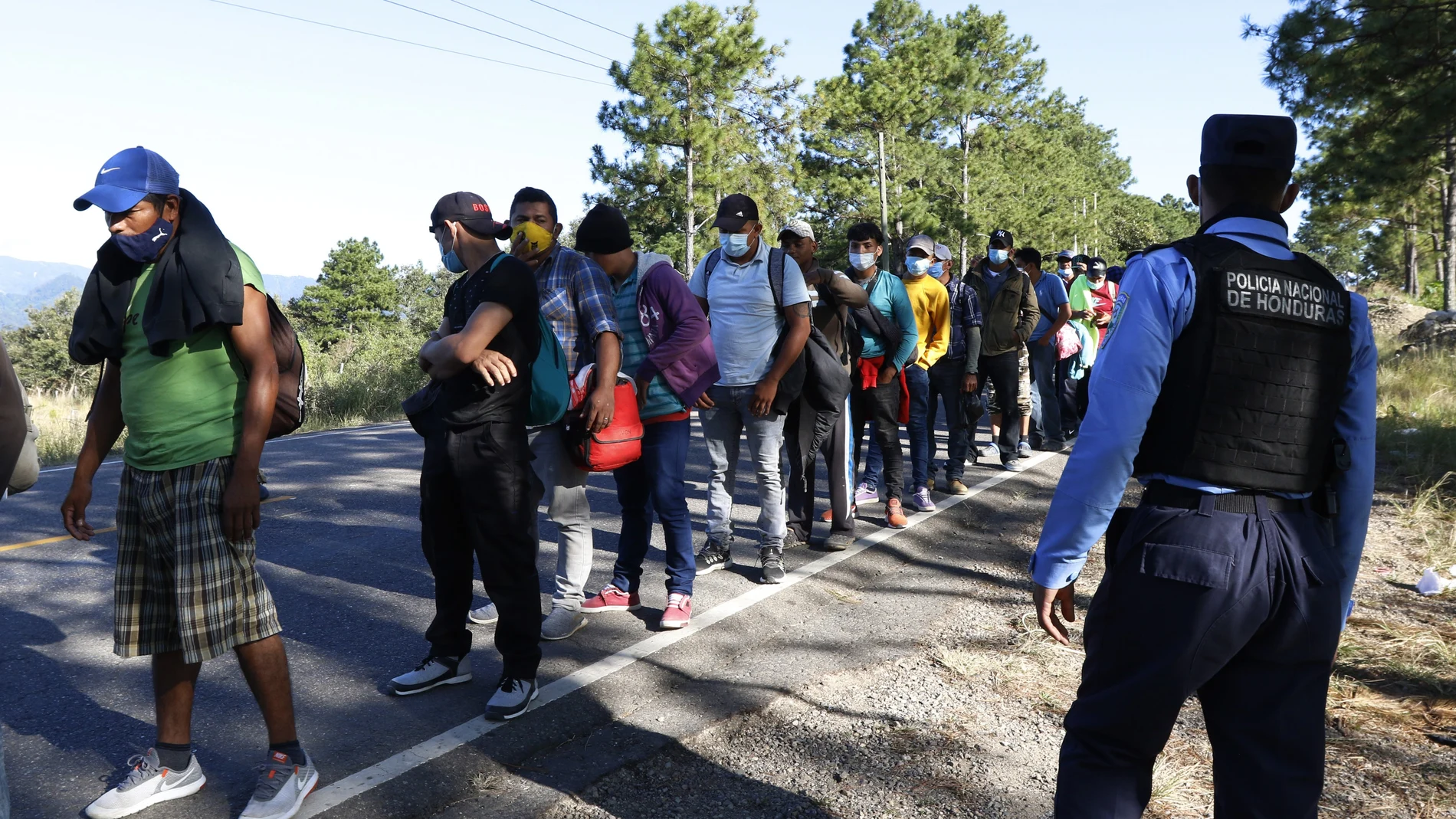 Migrants line up at a police checkpoint on their way North near Agua Caliente, close to the border with Guatemala, Thursday, Dec. 10, 2020. Honduran security forces stationed on the highway a few kilometers before Agua Caliente, asked the migrants for their passports or identity cards and proof of a COVID-19 test, and if they did not produce those documents they would not be allowed to move on. (AP Photo/Delmer Martinez)