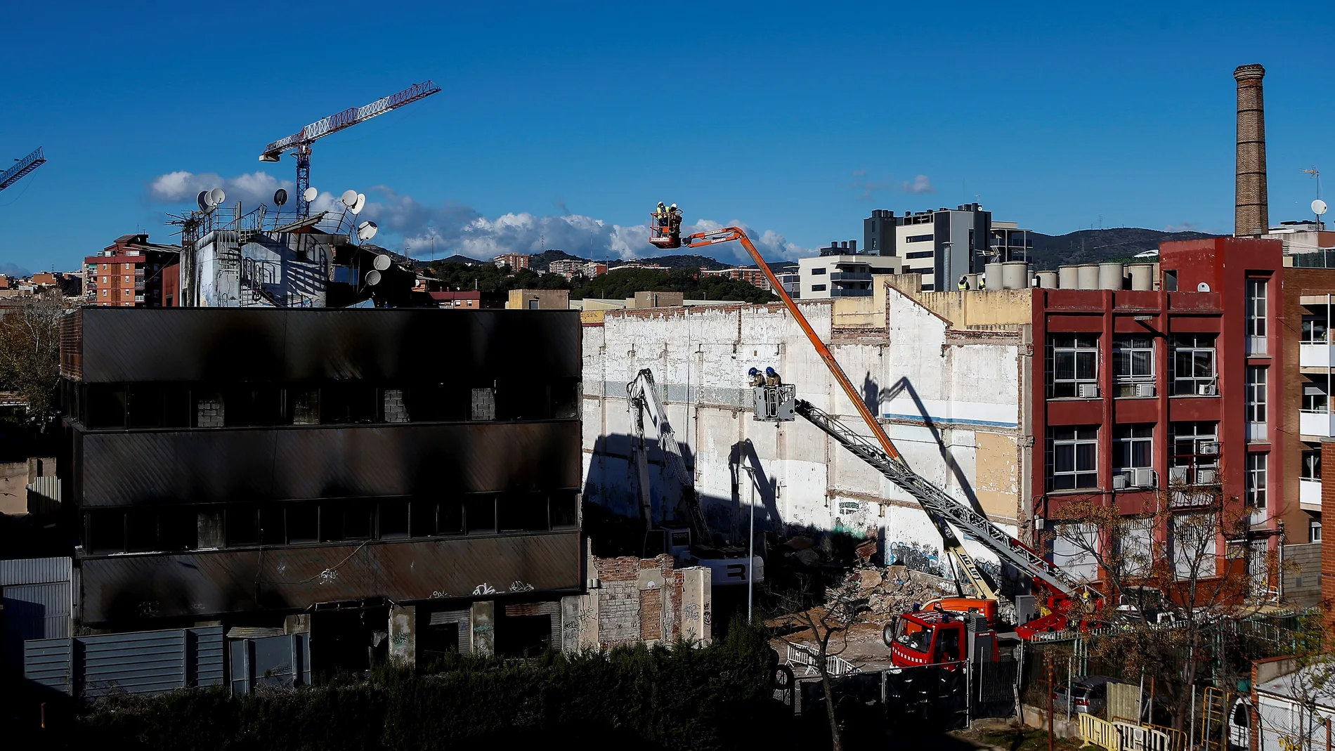 Bomberos de la Generalitat y trabajadores de la empresa de derribos inspeccionan en Badalona el inicio de la demolición de la nave donde murieron tres inmigrantes "sin techo" en un incendio. EFE/ Quique García