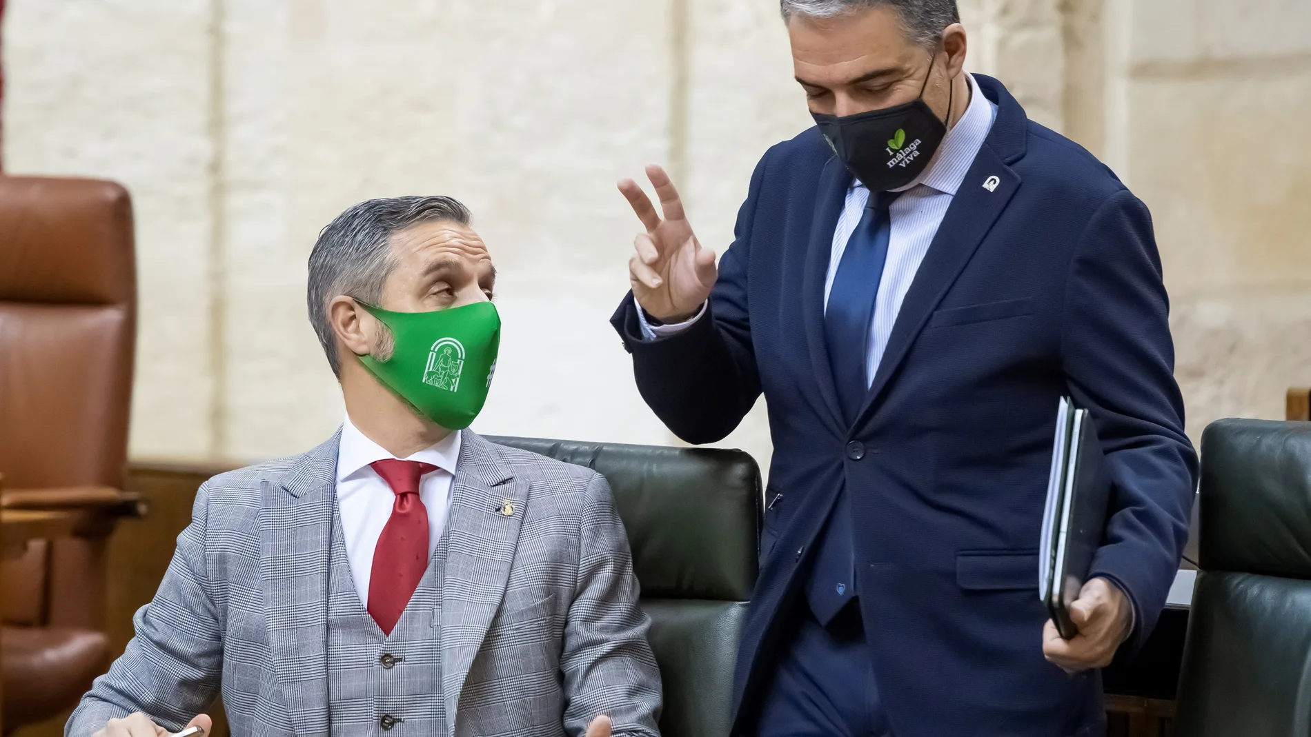 El consejero de la Presidencia, Elías Bendodo (d), conversa con el consejero de Hacienda, Juan Bravo (i), al inicio del pleno del Parlamento de Andalucía