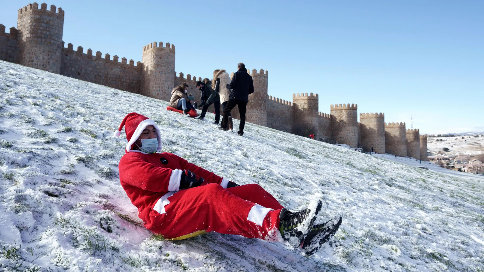 Un hombre disfrazado de Papá Noel se tira en trineo por el lienzo norte de la muralla de Ávila este viernes