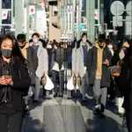 unos peatones con mascarillas se reflejan en un escaparate del distrito comercial de Ginza en Tokio, Japón