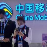 FILE - In this Oct. 14, 2020 file photo, staff members wearing face masks to protect against the spread of the coronavirus use their smartphones at a display from Chinese telecommunications firm China Mobile at the PT Expo in Beijing. The New York Stock Exchange is going ahead with plans to delist shares of three Chinese state-owned phone carriers under an executive order from President Donald Trump. The exchange said trading in the three companies, China Telecom Corp. Ltd., China Mobile Ltd. and China Unicom Hong Kong Ltd., will be suspended after the markets close on Jan. 11, 2021. (AP Photo/Mark Schiefelbein, File)