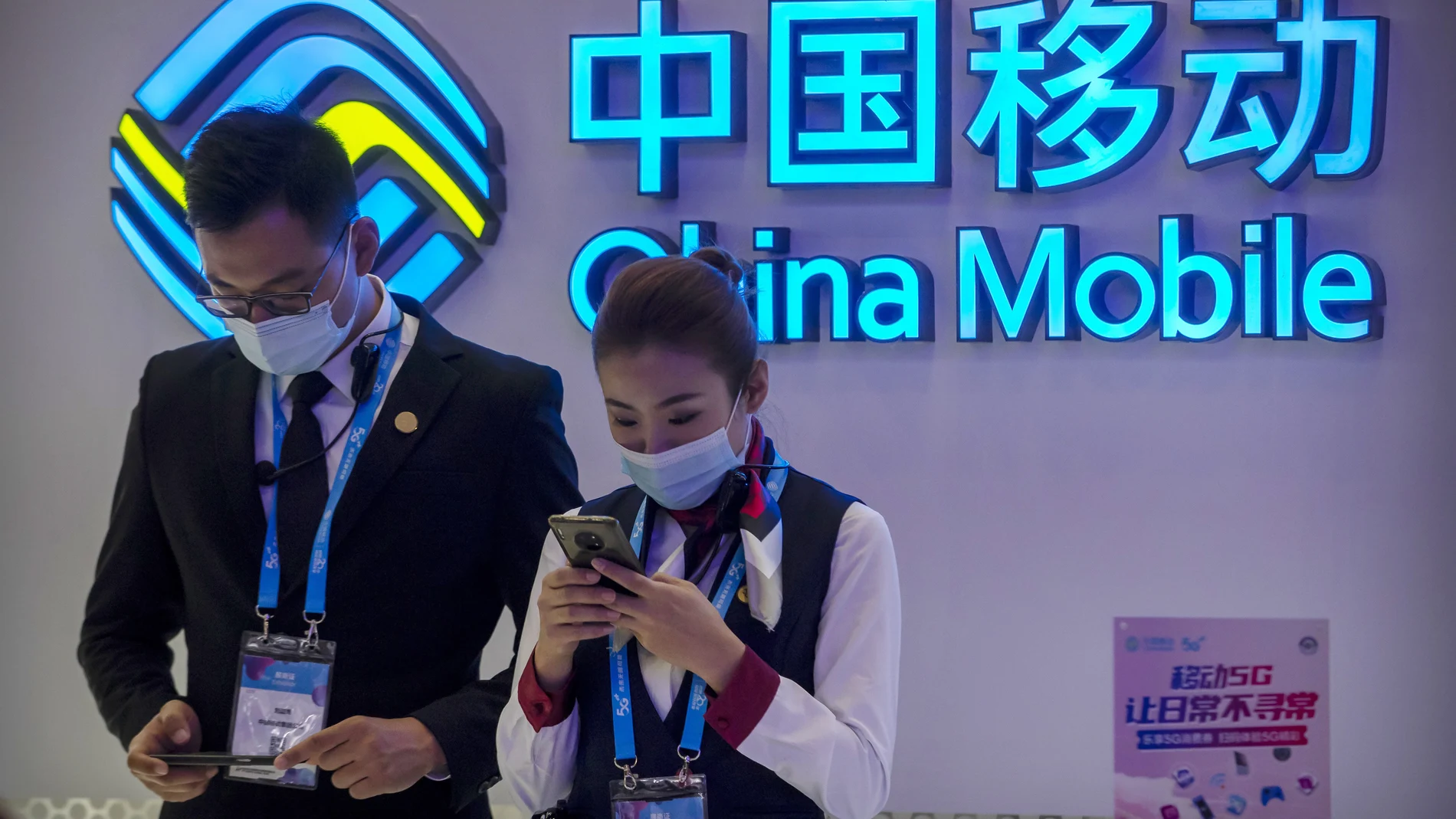 FILE - In this Oct. 14, 2020 file photo, staff members wearing face masks to protect against the spread of the coronavirus use their smartphones at a display from Chinese telecommunications firm China Mobile at the PT Expo in Beijing. The New York Stock Exchange is going ahead with plans to delist shares of three Chinese state-owned phone carriers under an executive order from President Donald Trump. The exchange said trading in the three companies, China Telecom Corp. Ltd., China Mobile Ltd. and China Unicom Hong Kong Ltd., will be suspended after the markets close on Jan. 11, 2021. (AP Photo/Mark Schiefelbein, File)