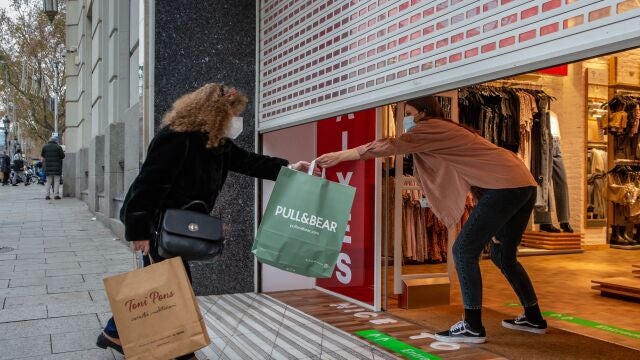 Una clienta recoge una bolsa de manos de una dependienta en un comercio del centro de Barcelona, este jueves en que en Cataluña arrancan las rebajas de enero el mismo día que entran en vigor las nuevas restricciones de la Generalitat, que han llevado a cerrar los centros comerciales.
