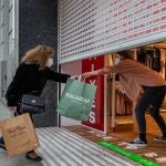 Una clienta recoge una bolsa de manos de una dependienta en un comercio del centro de Barcelona, este jueves en que en Cataluña arrancan las rebajas de enero el mismo día que entran en vigor las nuevas restricciones de la Generalitat, que han llevado a cerrar los centros comerciales.