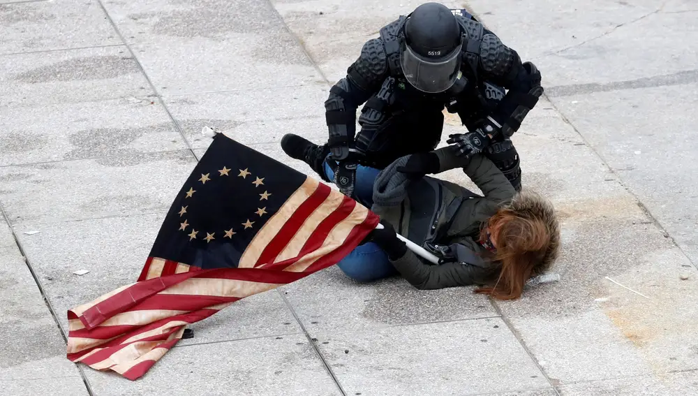 Un policía reduce a un manifestante con una bandera de EE UU