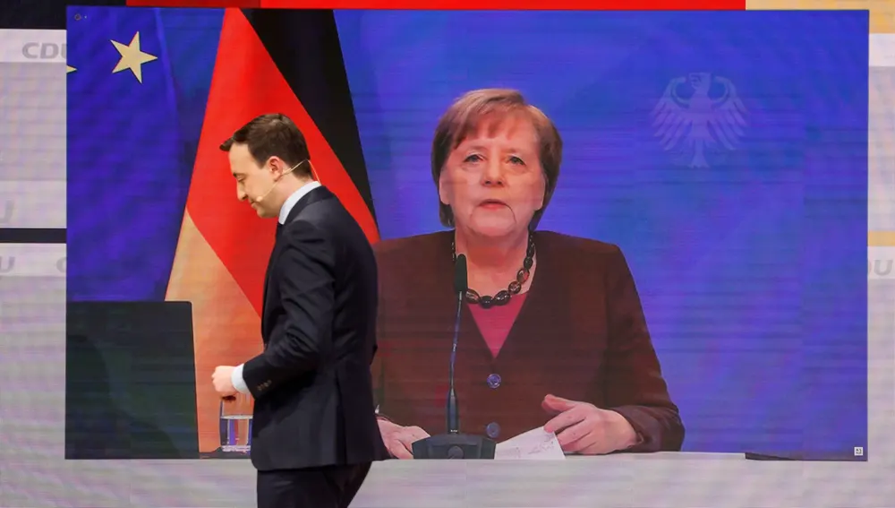 El secretario general de la CDU, Paul Ziemiak, pasa por la pantalla en la que se ve a la canciller Merkel durante el 33 Congreso de la formación democristiana