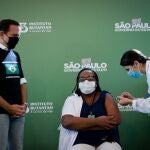 AME9923. SAO PAULO (BRASIL), 17/01/2021.- Mônica Calazans (c), enfermera del Hospital las Clínicas de la capital paulista recibe la vacuna contra la covid-19 en presencia del gobernador de Sao Paulo, Joao Doria (i), hoy, en Sao Paulo (Brasil). Brasil, uno de los países del mundo más afectados por la pandemia del coronavirus, aplicó este domingo en Sao Paulo la primera dosis de la vacuna contra la covid-19 a la enfermera de 54 años, en momentos en los que el gigante latinoamericano enfrenta una segunda ola de la enfermedad. La primera dosis de la vacuna desarrollada por el laboratorio chino Sinovac y el Instituto brasileño Butantan fue aplicada tan solo minutos después de la aprobación de su uso de emergencia por parte de la Agencia Nacional de Vigilancia Sanitaria (Anvisa). EFE/ Fernando Bizerra Jr