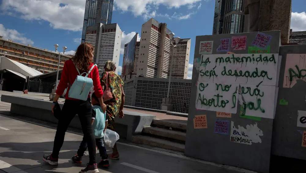 Varias personas caminan frente a un grafiti que dice &quot;La maternidad será deseada o no será. Aborto legal&quot; en una pared, el 16 de enero de 2021, en Caracas (Venezuela)