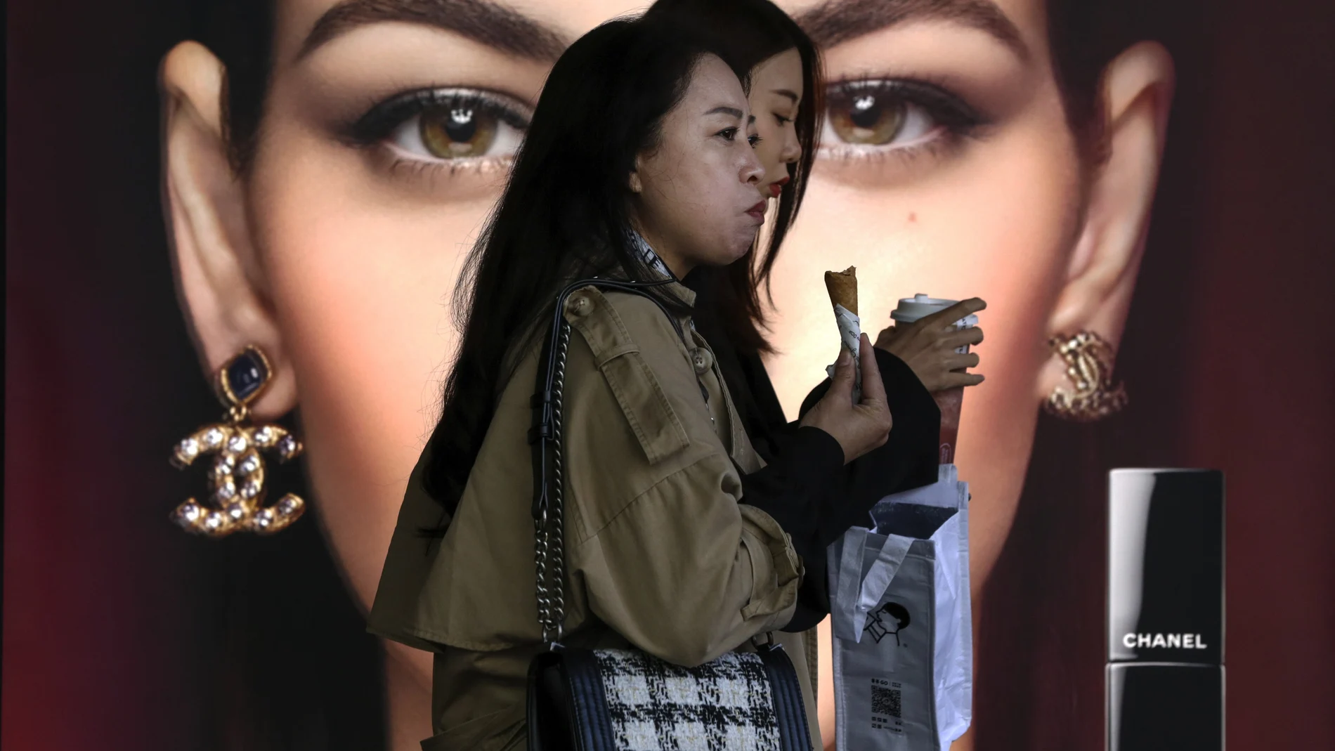 FILE - In this Oct. 19, 2020, file photo, women eating snack walk by a Chanel cosmetic shop at the capital city's popular shopping mall in Beijing. China’s economy grew 2.3% in 2020 as a recovery from the coronavirus pandemic accelerated while the United States, Europe and Japan struggled with disease flare-ups. (AP Photo/Andy Wong, File)