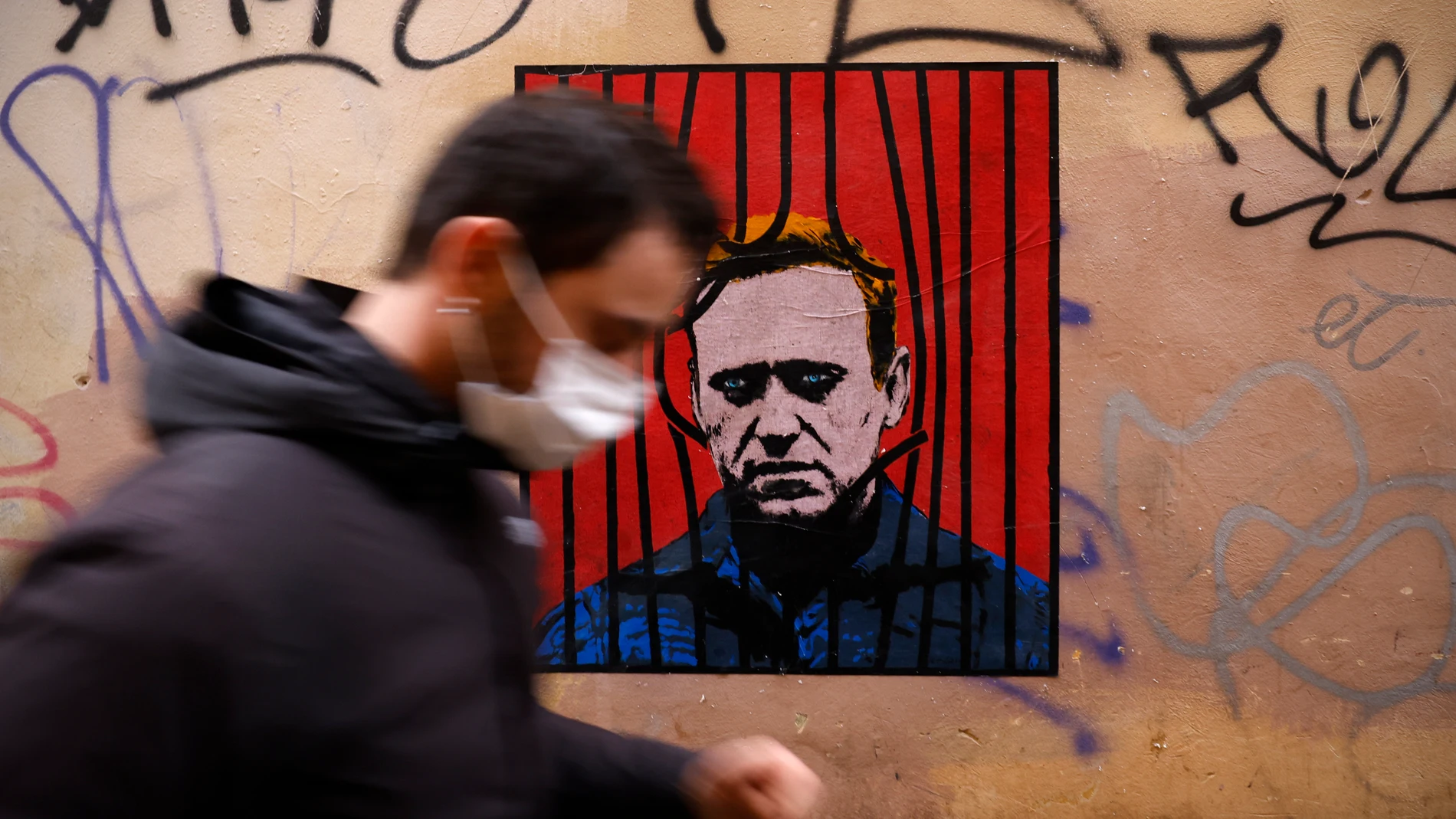 Un hombre con mascarilla pasa delante de un póster de Alexei Navalni en Roma